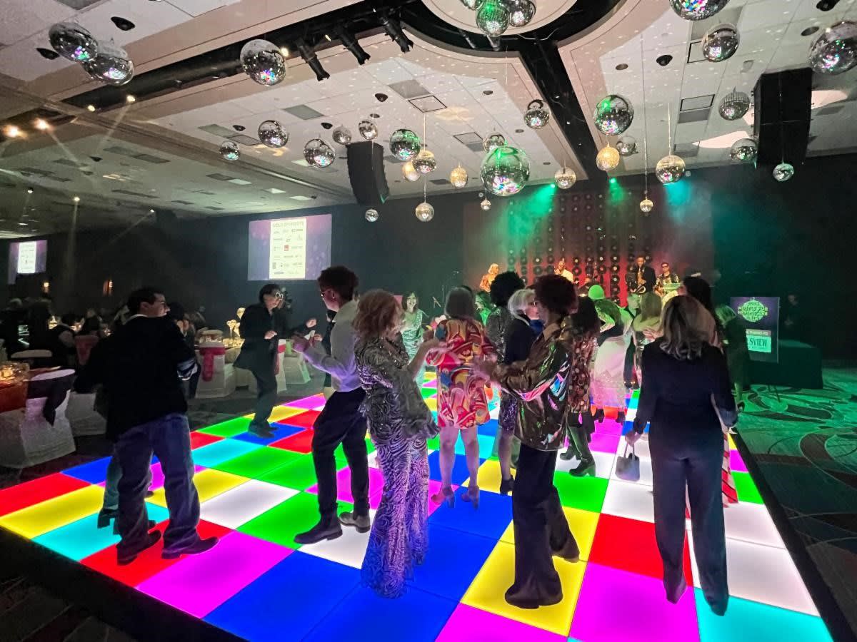 People dance on a colourful checkerboard dance floor