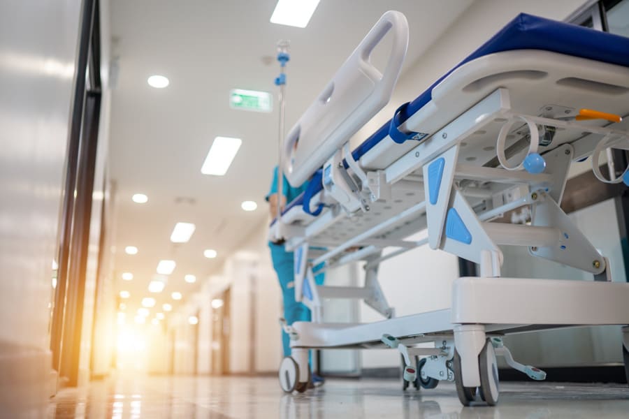 A person in scrubs pushes a hospital gurney through a hospital hallway