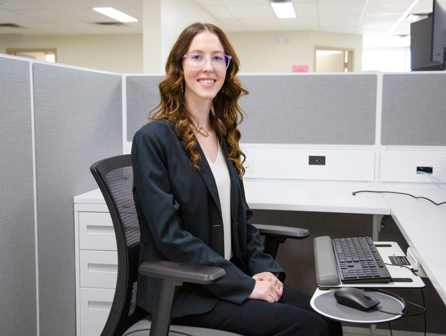 Julia Becevel sits at a computer cubicle in the HIS office. 