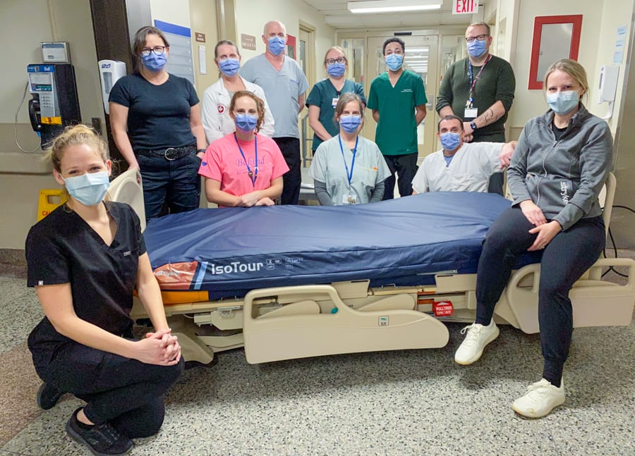 A group of healthcare workers gather around a hospital bed equipped with a gel mattress.